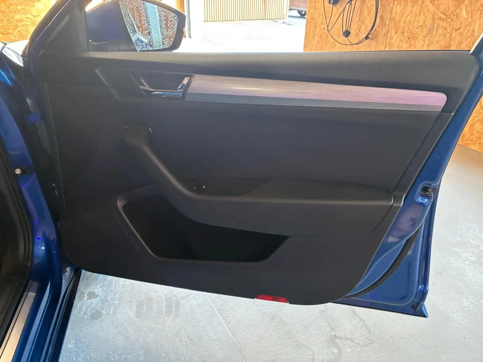 Vue intérieure de la porte avant gauche d'une Skoda Superb Combi bleu 2021 avec garniture noire et insert bois clair.