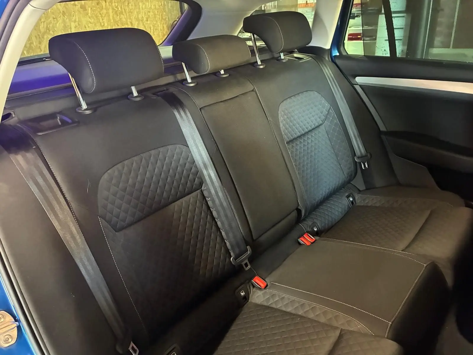 Vue intérieure de la banquette arrière noire en tissu matelassé du Skoda Superb Combi bleu, avec ceintures et appuie-têtes.