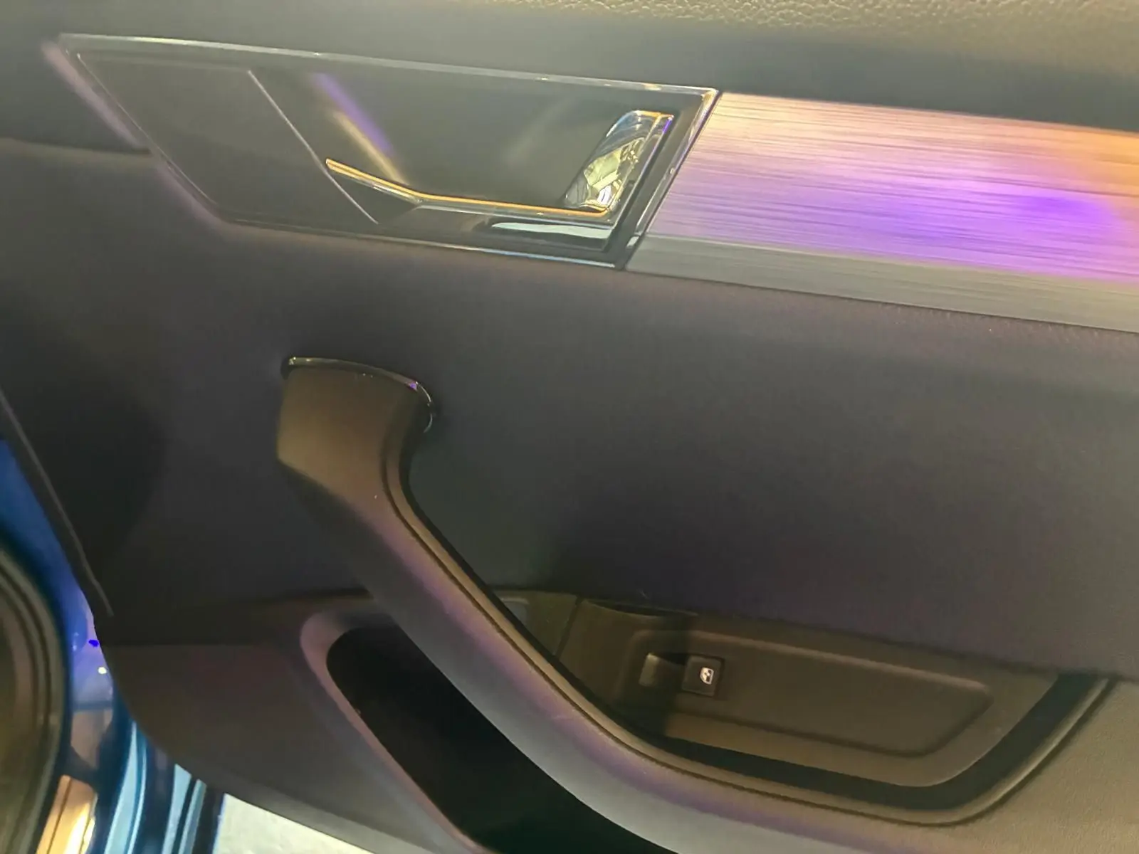 Gros plan sur la porte intérieure côté gauche d’une Skoda Superb Combi bleu, avec poignée noire et insert décoratif argenté.
