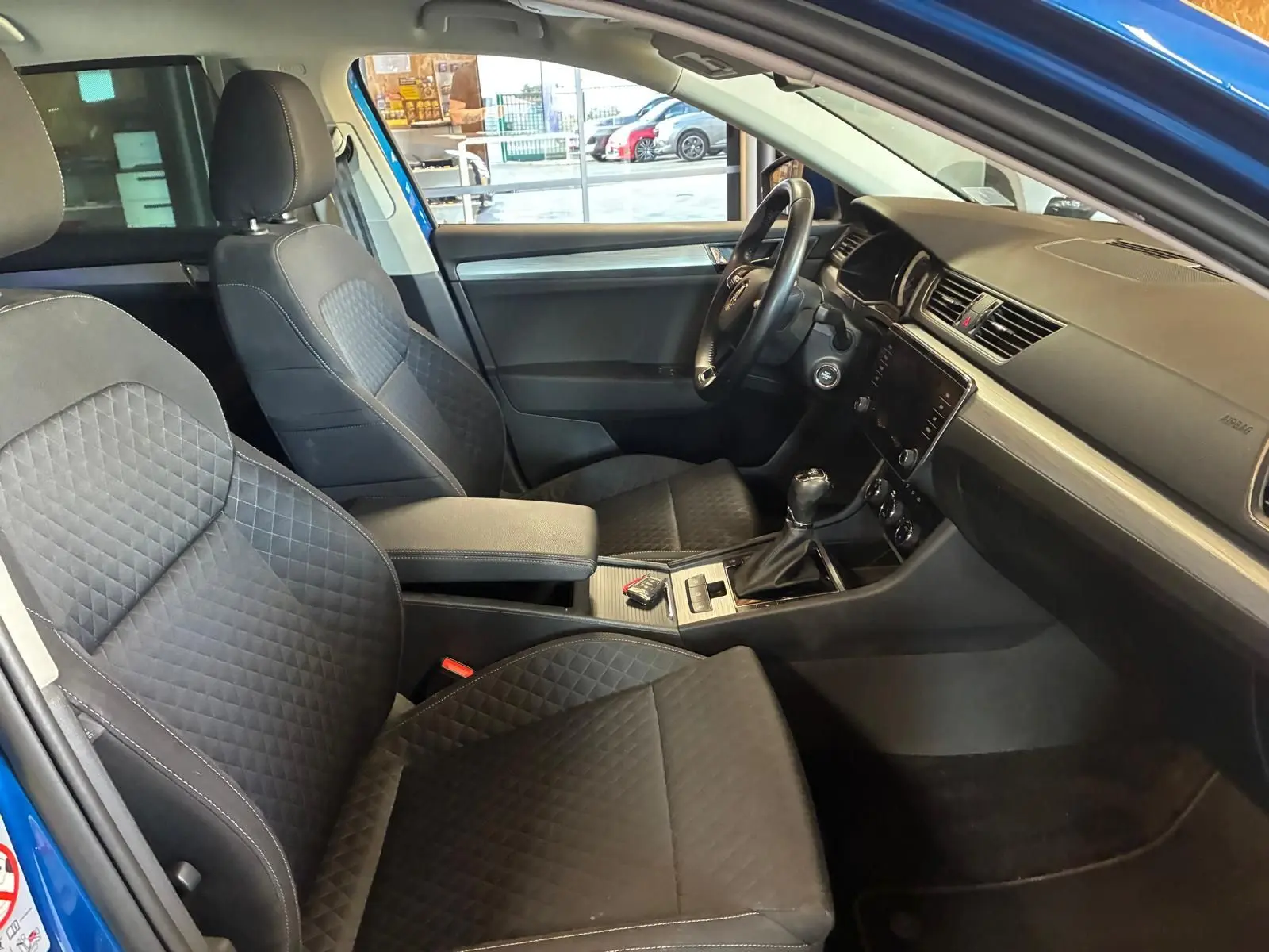 Vue intérieure côté conducteur de la Skoda Superb Combi 2021 bleu, sièges tissu noir avec console centrale et volant visibles.