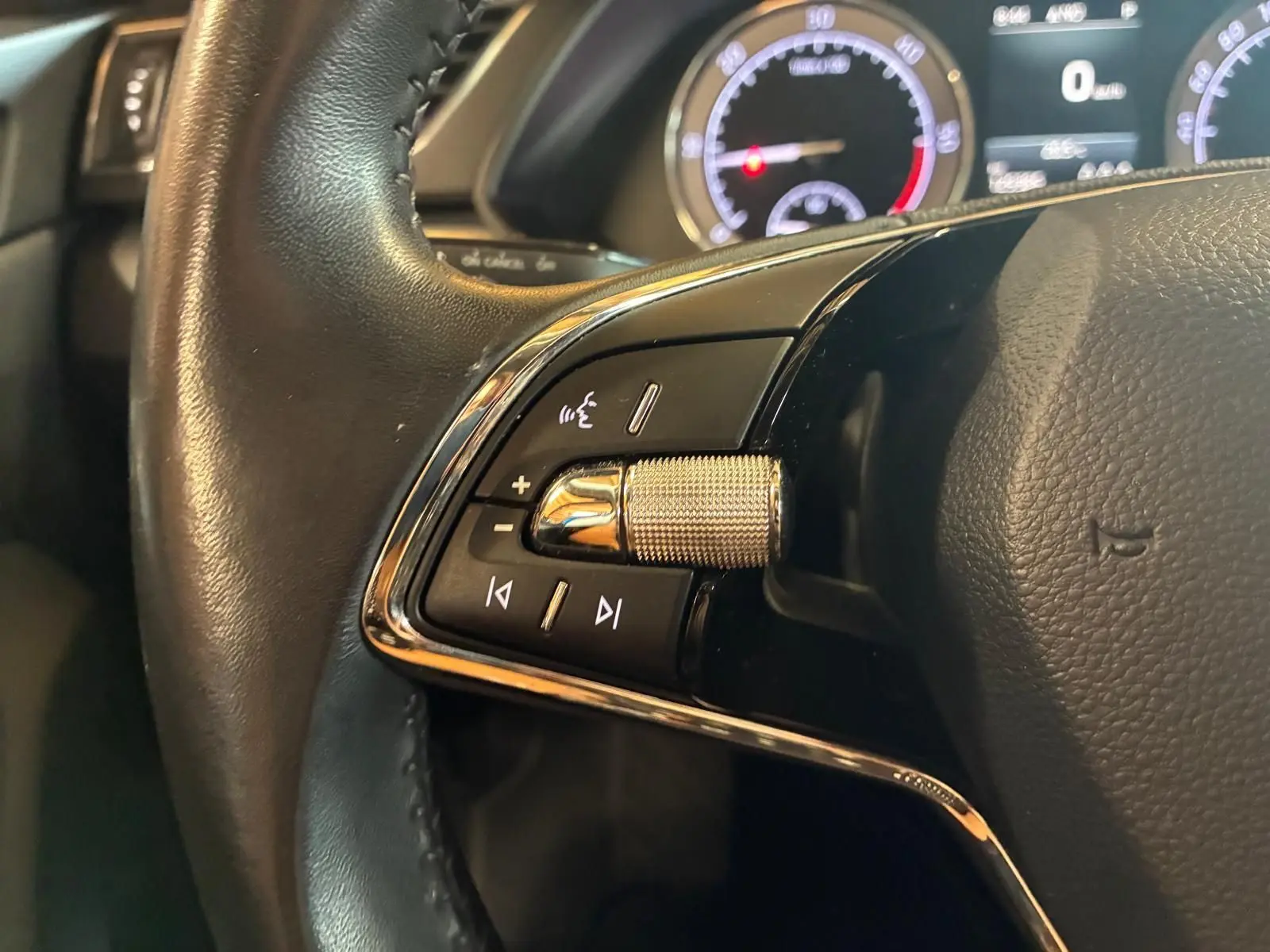 Gros plan sur les commandes gauche du volant noir d’une Skoda Superb Combi 2021 avec tableau de bord numérique en arrière-plan.