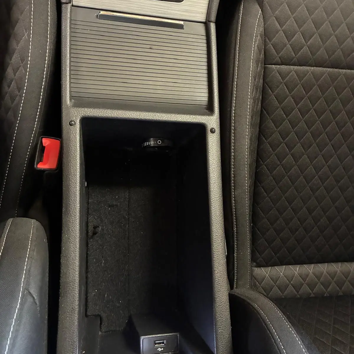 Vue rapprochée de la console centrale noire avec rangement ouvert et sièges tissu noir à surpiqûres blanches dans une Skoda Superb Combi.