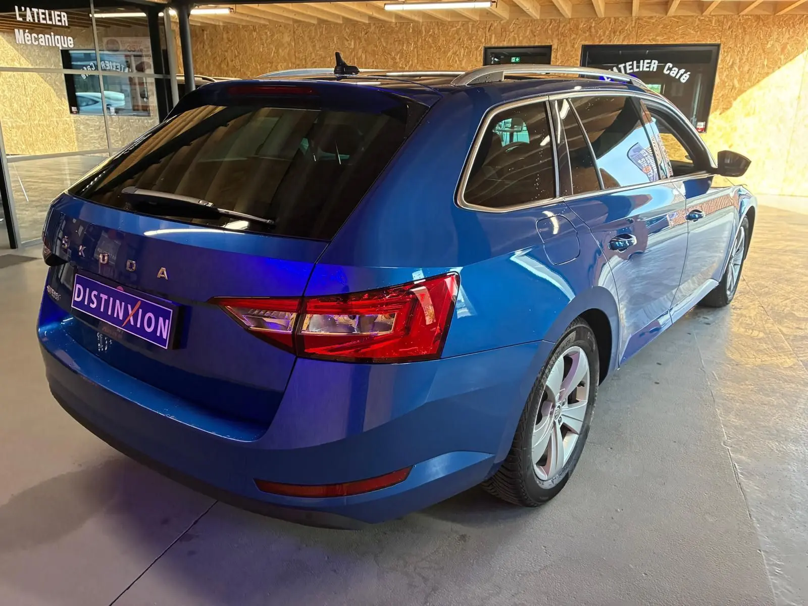 Vue 3/4 arrière droite d'une Skoda Superb Combi bleu métallisé, break diesel 5 portes en intérieur showroom.