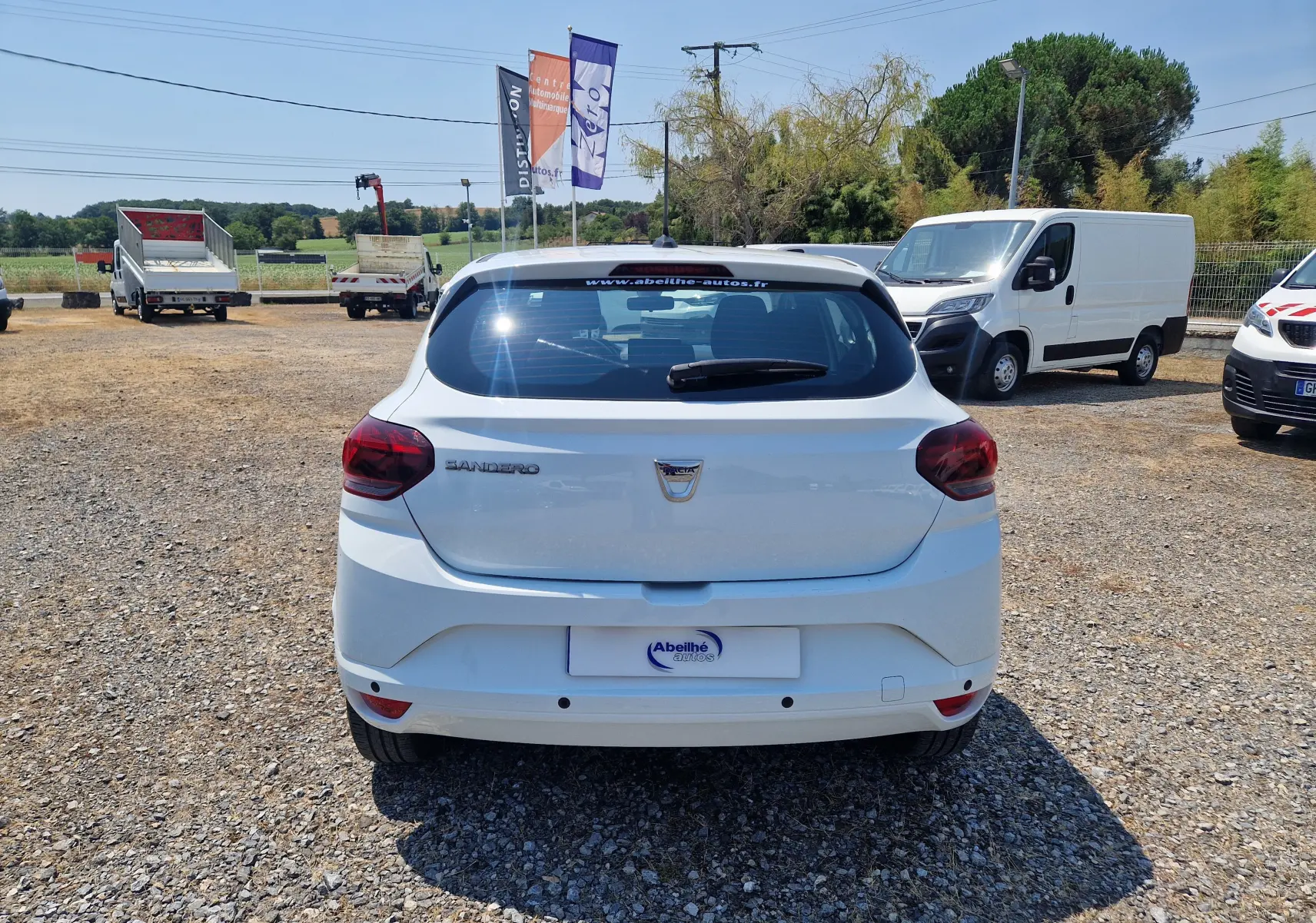 Vue arrière d'une Dacia Sandero blanche 2022, avec feux arrière rouges et logo Dacia visible sur le hayon.