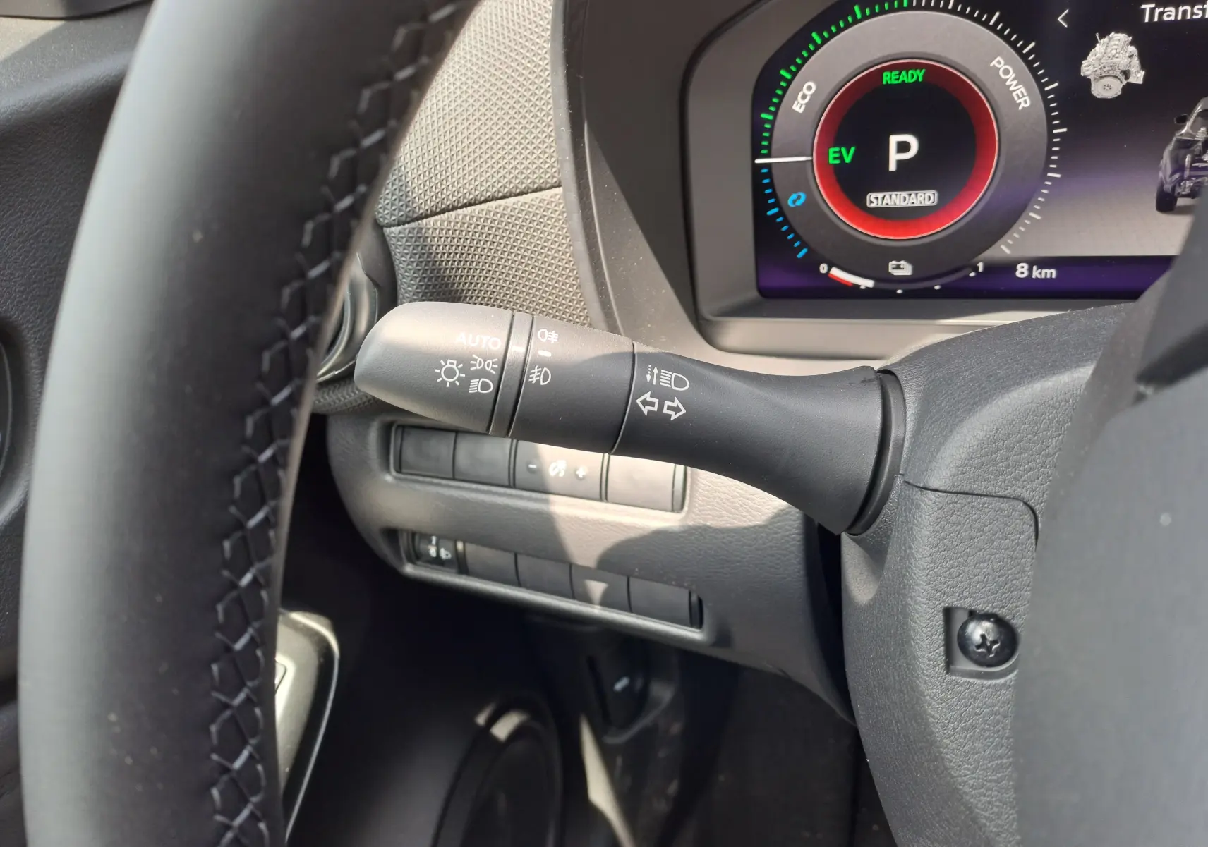 Gros plan sur la manette des clignotants à gauche du volant du Nissan Juke Hybrid gris, avec tableau de bord numérique visible.