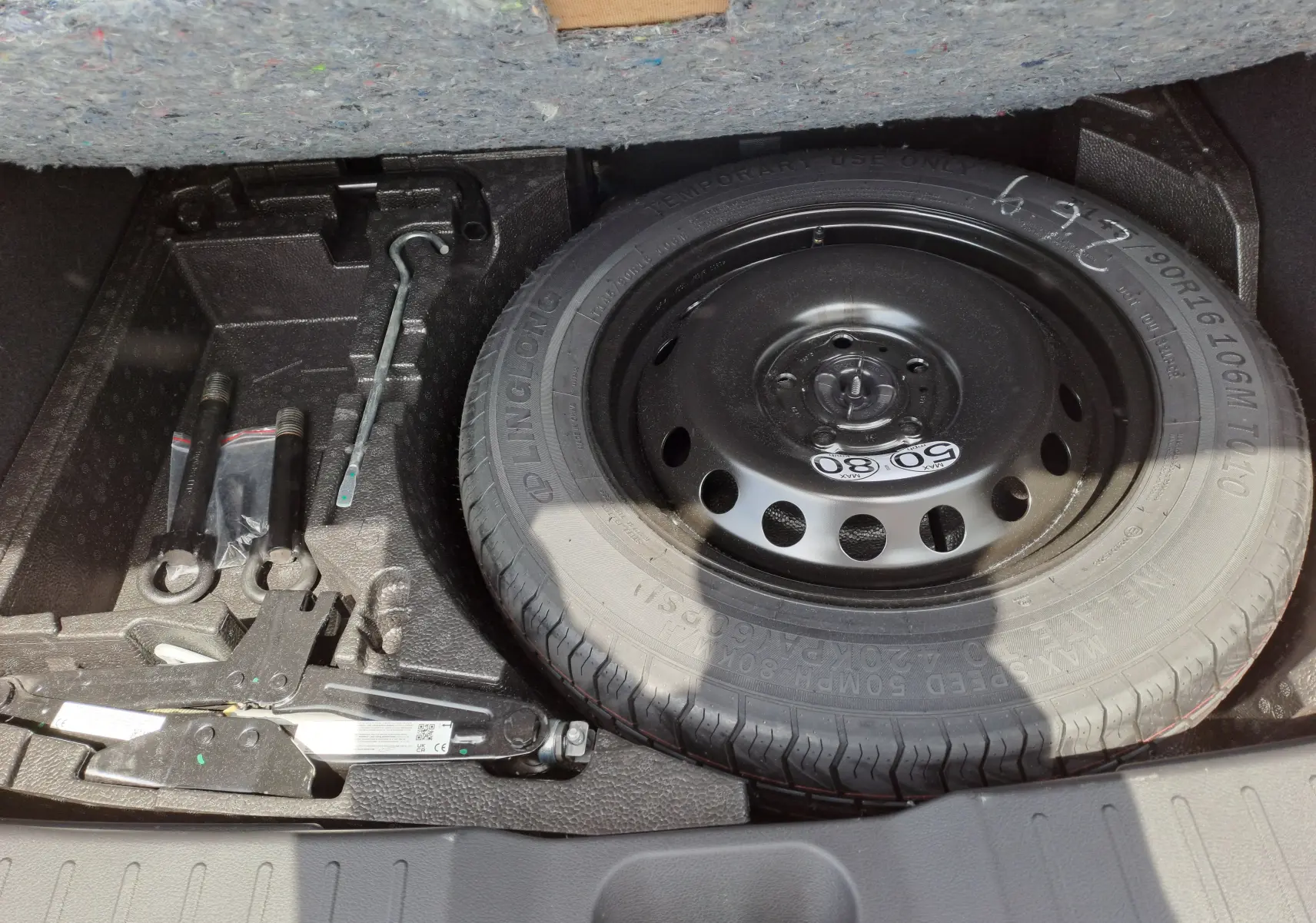 Vue du coffre du Nissan Juke Hybrid 2025 montrant la roue de secours et les outils de dépannage rangés sous le plancher.