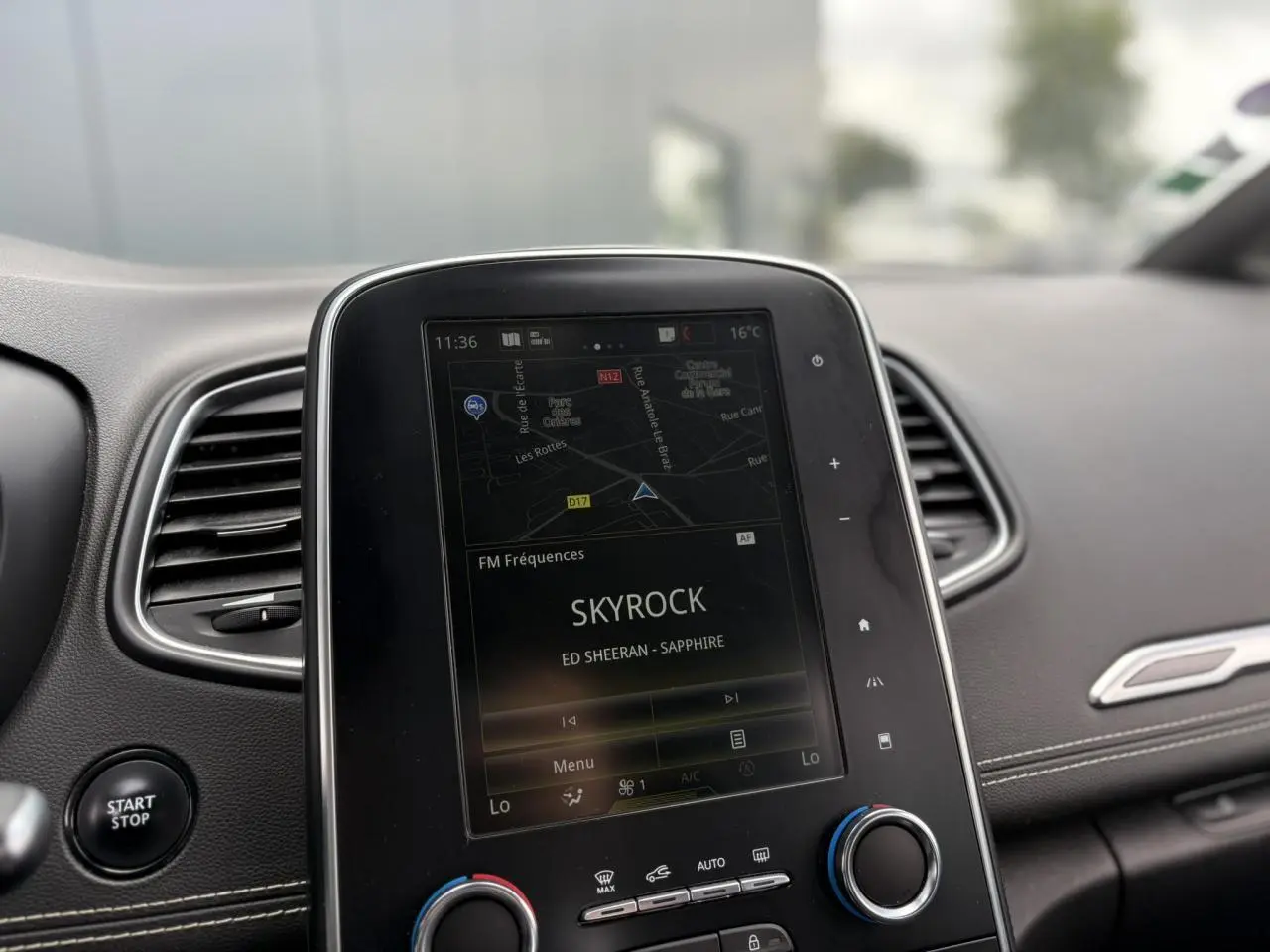 Vue rapprochée de la console centrale du Renault Grand Scenic blanc nacré, écran tactile affichant la radio Skyrock.