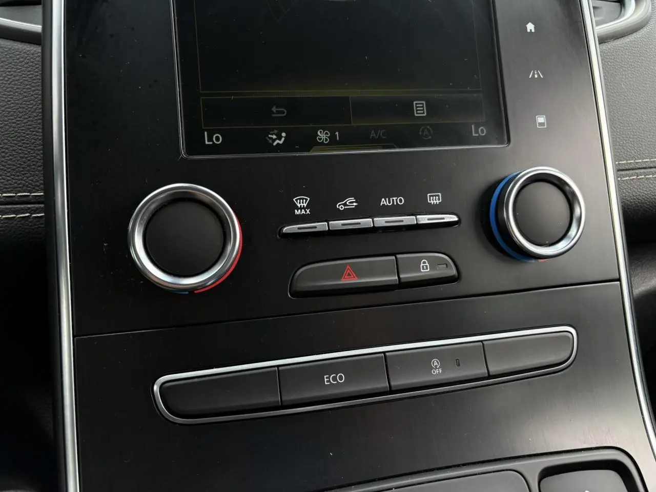 Gros plan sur la console centrale noire du Renault Grand Scenic IV blanc nacré, avec commandes climatisation et bouton Eco visibles.