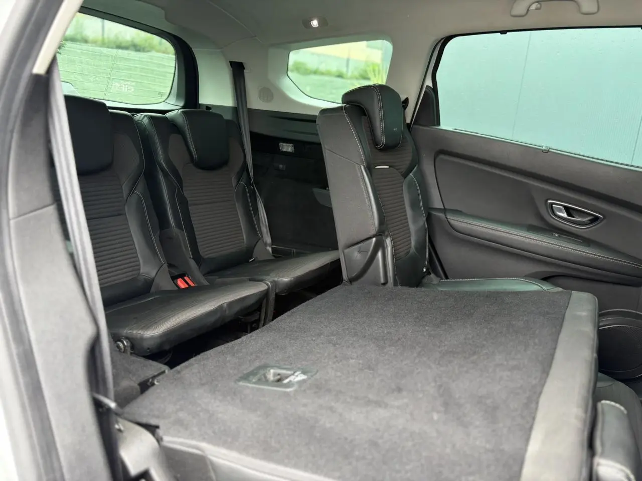 Vue intérieure côté droit du Renault Grand Scenic IV montrant les sièges arrière noirs et une banquette rabattue.
