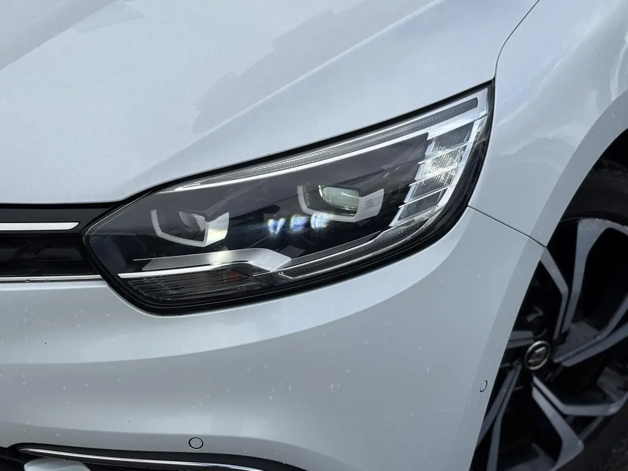 Gros plan sur le phare avant droit blanc nacré du Renault Grand Scenic IV avec jante alliage noire et argentée