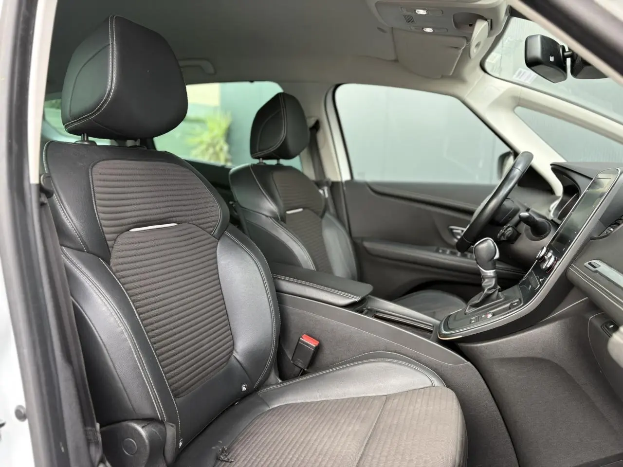 Vue intérieure côté conducteur du Renault Grand Scenic blanc nacré, sièges noirs en cuir et tissu avec console centrale visible.