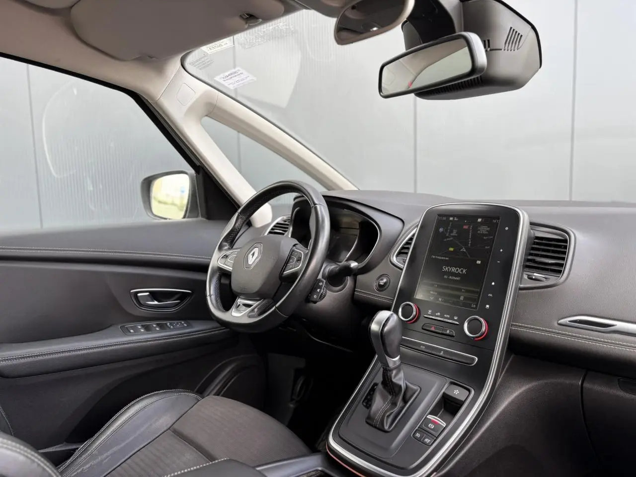 Vue intérieure côté conducteur du Renault Grand Scenic IV avec tableau de bord noir et écran tactile central allumé.