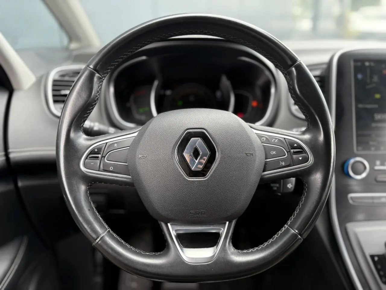Volant en cuir noir avec logo Renault au centre, tableau de bord et écran tactile du Renault Grand Scenic IV visibles en arrière-plan.