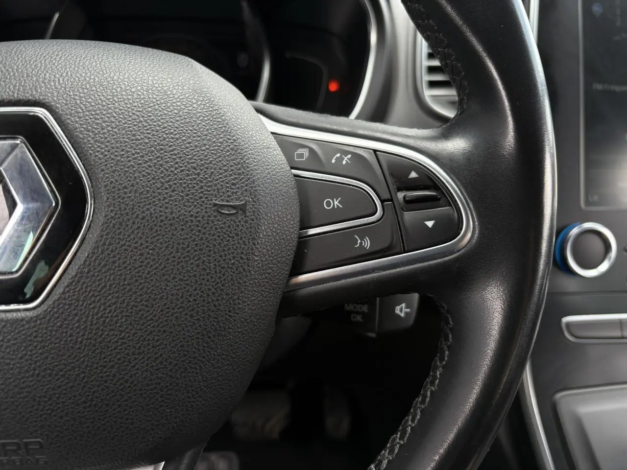 Gros plan sur le volant cuir noir du Renault Grand Scenic IV avec commandes intégrées et logo central chromé.