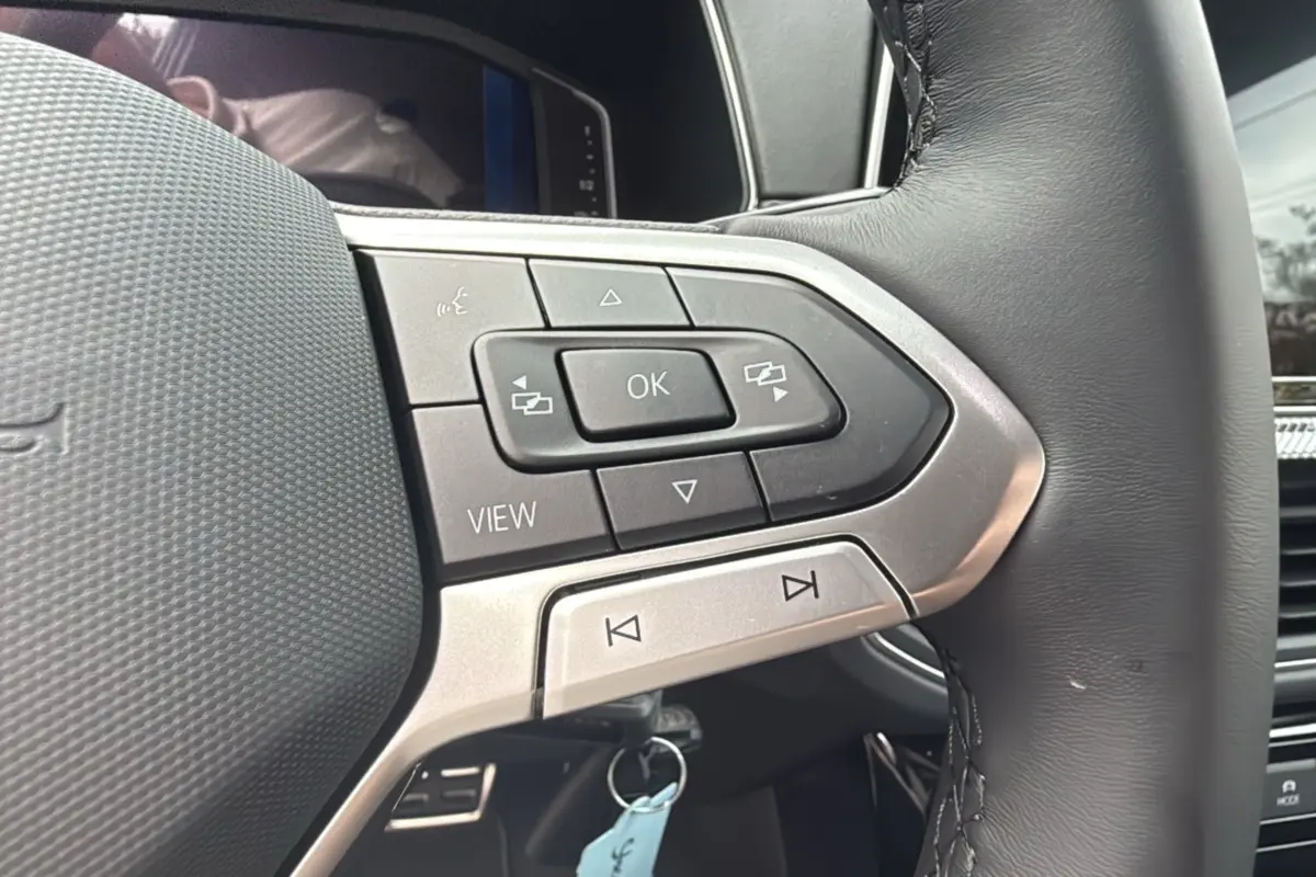 Gros plan sur les commandes multifonctions du volant cuir du Volkswagen T-cross blanc pur, version TSI 116 DSG7 R-LINE 2025.