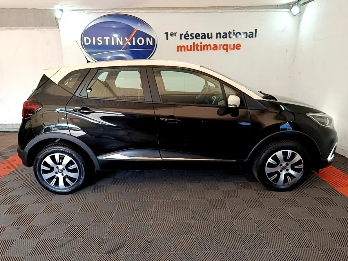 Profil droit d'un Renault Captur Business noir avec toit blanc, jantes alliage et feux arrière visibles en intérieur showroom.