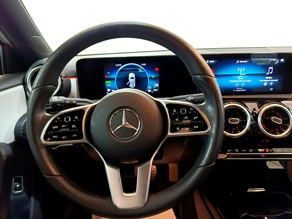 Vue intérieure centrée sur le volant cuir multifonctions et le tableau de bord numérique de la Mercedes Classe A blanche.