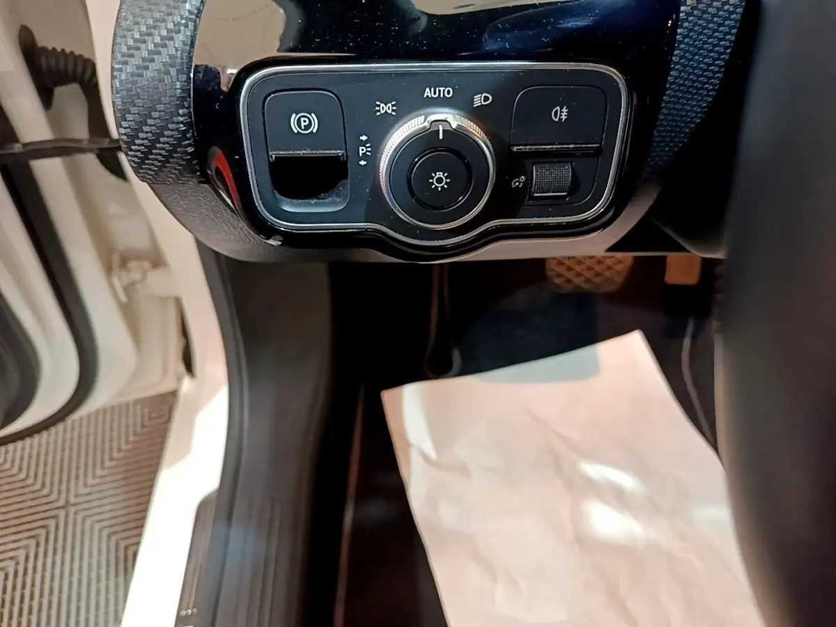 Gros plan sur le panneau de commande des feux et du frein de stationnement d'une Mercedes Classe A blanche, vue côté conducteur.