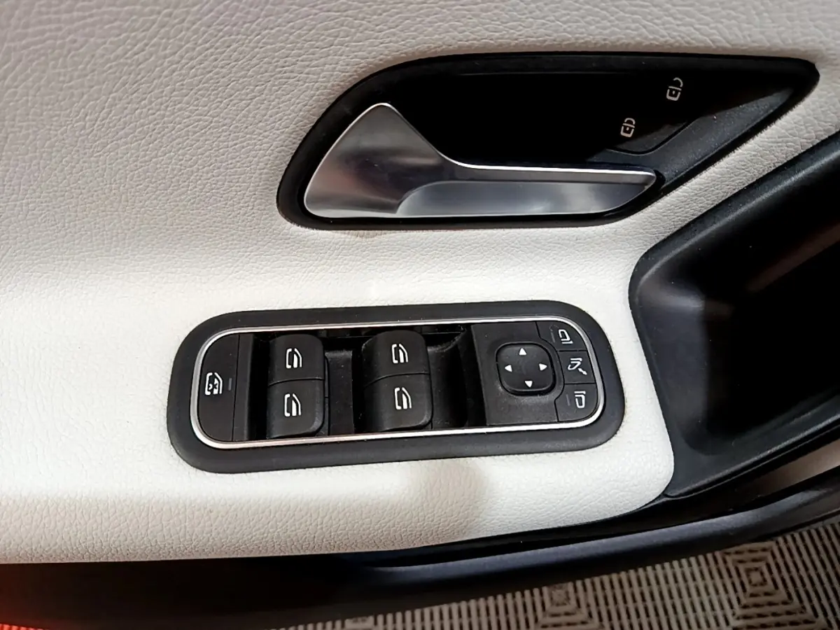 Gros plan sur la commande des vitres et la poignée de porte côté conducteur en cuir blanc de la Mercedes Classe A Berline.