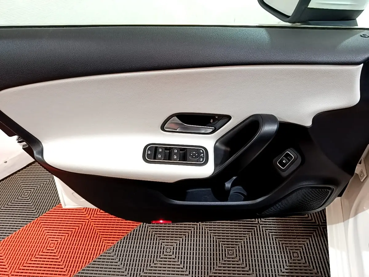 Gros plan sur la porte avant gauche blanche d'une Mercedes Classe A 250 e Business Line, avec commandes électriques et garniture bicolore.