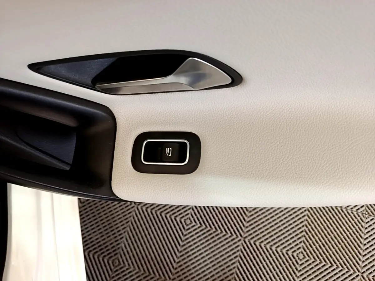 Détail de la poignée intérieure et bouton de lève-vitre sur la porte côté gauche d'une Mercedes Classe A blanche.