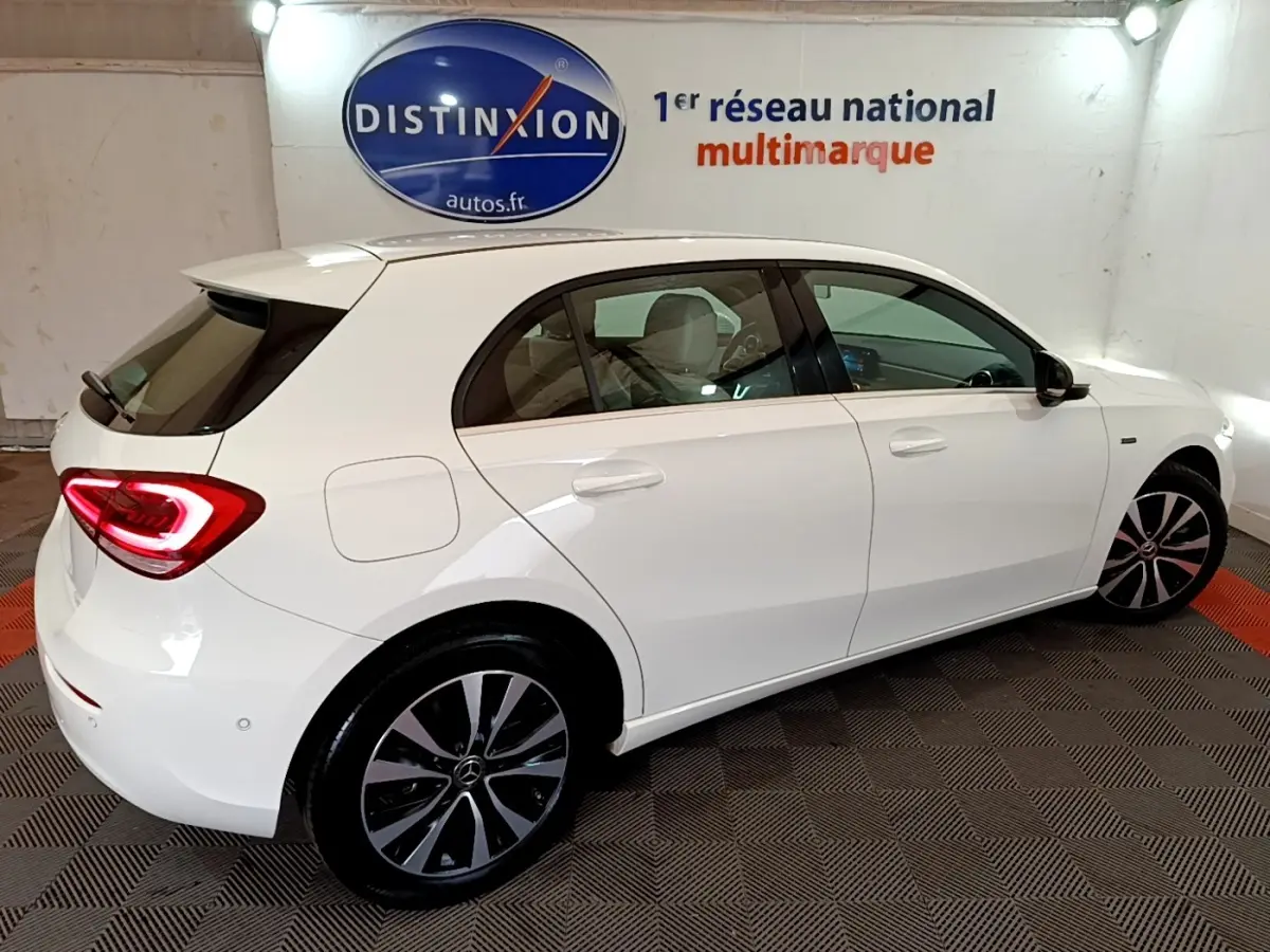 Vue côté droit arrière d'une Mercedes Classe A Berline blanche avec feux arrière LED allumés dans un showroom.