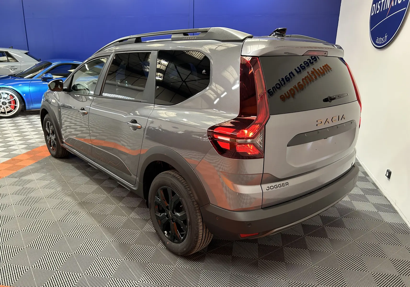 Vue 3/4 arrière droite du Dacia Jogger gris schiste métallisé avec jantes noires et vitres teintées en intérieur showroom.