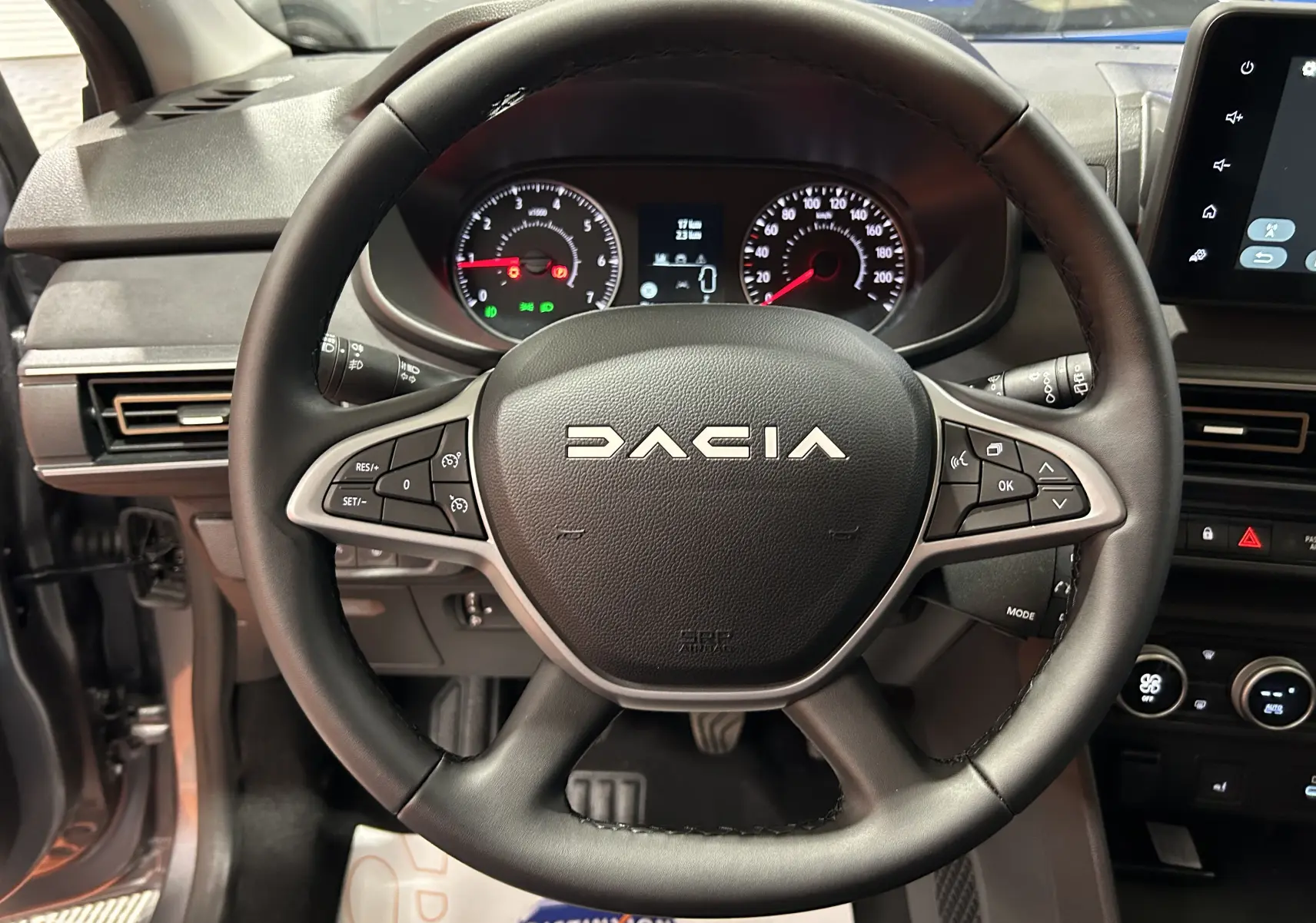 Vue rapprochée du volant noir de la Dacia Jogger gris schiste, avec tableau de bord et commandes visibles.