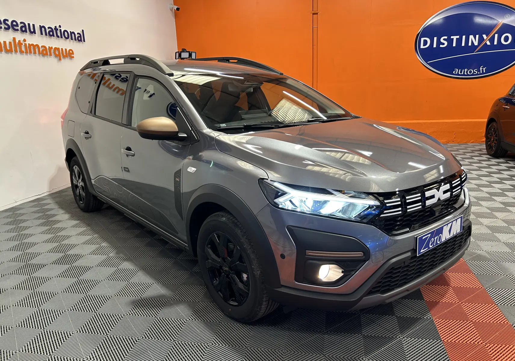 Vue 3/4 avant d'un Dacia Jogger gris schiste métal avec jantes noires et rétroviseurs couleur or mat.