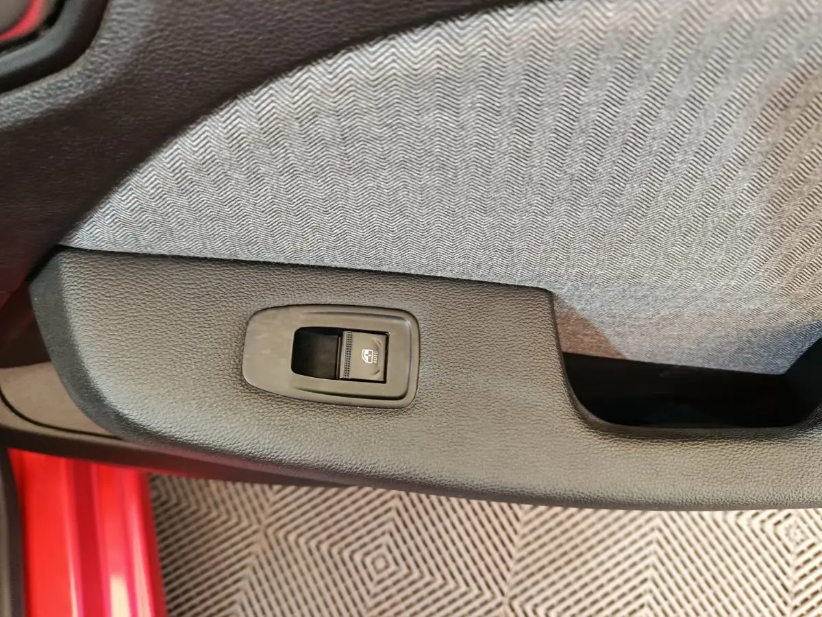 Détail de la commande de lève-vitre sur la porte intérieure côté conducteur d'une Renault Clio rouge 2024.