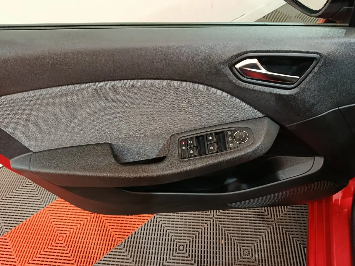 Vue intérieure du panneau de porte avant gauche de la Renault Clio rouge 2024 avec commandes électriques des vitres et verrouillage.