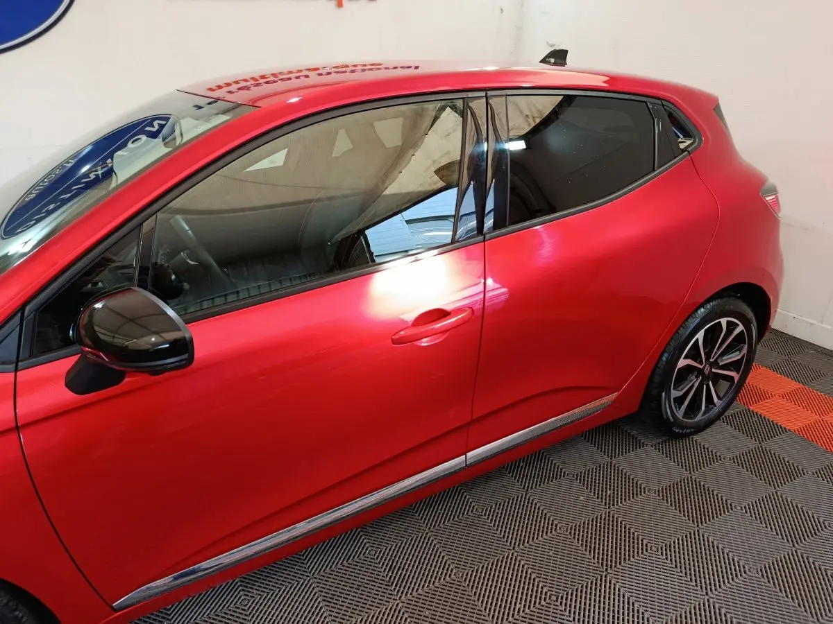 Profil droit d'une Renault Clio rouge 2024 avec rétroviseur noir brillant et jantes alliage distinctives.