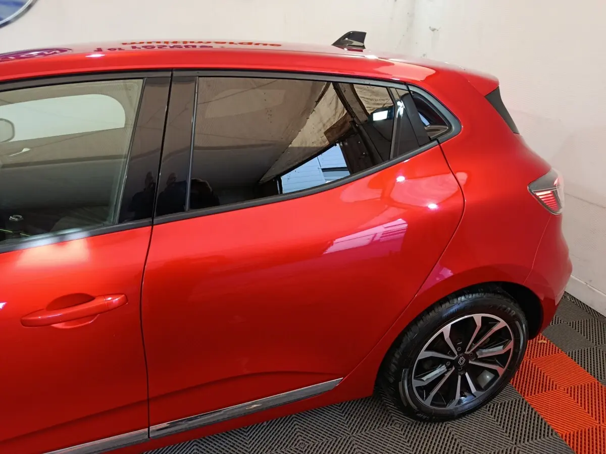 Vue latérale droite d'une Renault Clio rouge 2024, mettant en valeur la porte arrière et la jante alliage.