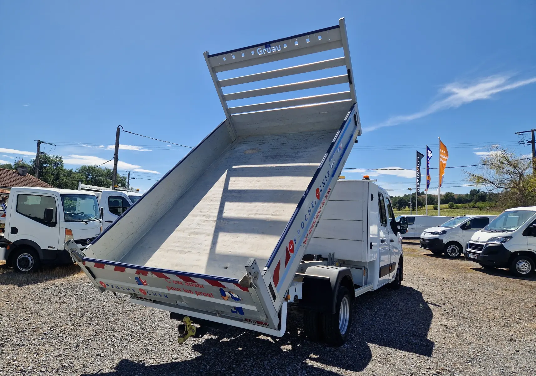 Renault Master Chassis double cabine blanc vu 3/4 arrière avec benne relevée et coffre latéral sur terrain extérieur.