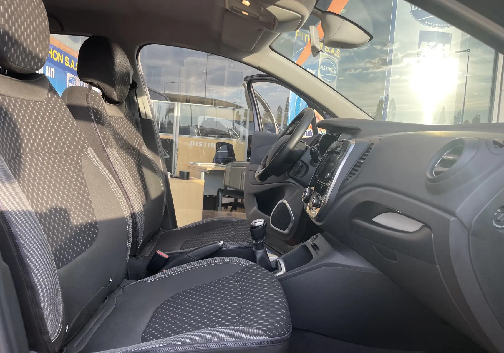 Intérieur avant du Renault Captur noir étoile, sièges tissu gris beige et tableau de bord avec console centrale visible.