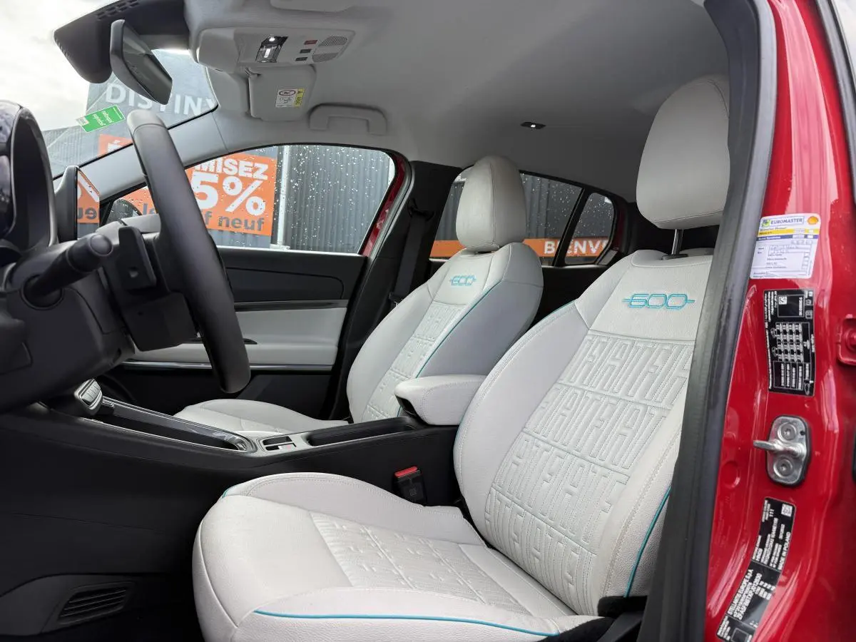 Intérieur de la FIAT 600 La Prima rouge, vue côté conducteur, sièges ivoire avec monogrammes bleus 600 et ECO.