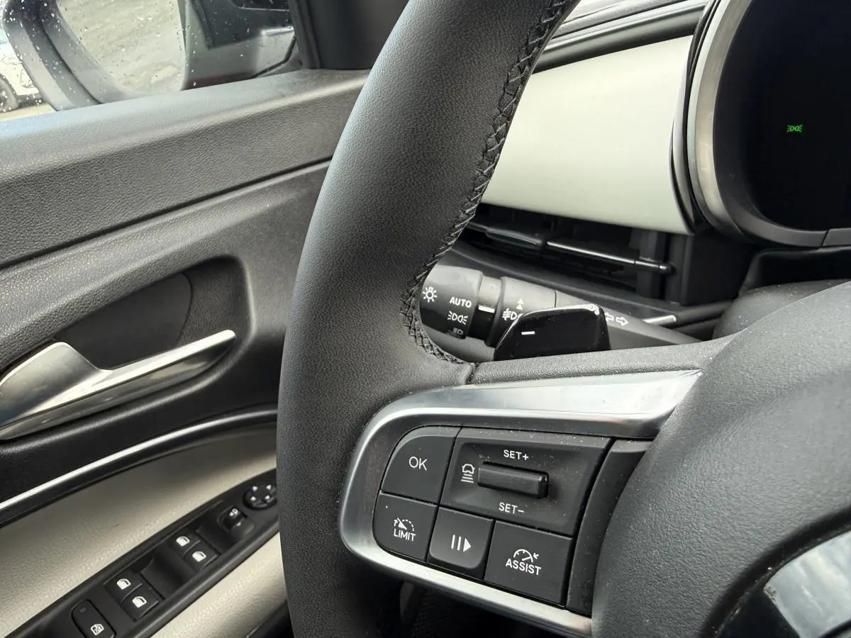 Gros plan sur le volant côté gauche et la portière ivoire de la FIAT 600 La Prima 2024, avec commandes intégrées.