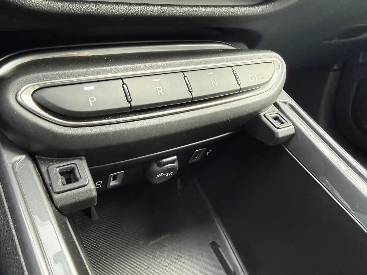 Gros plan sur la console centrale noire du Fiat 600 La Prima 2024, avec boutons de boîte auto et prises USB visibles.