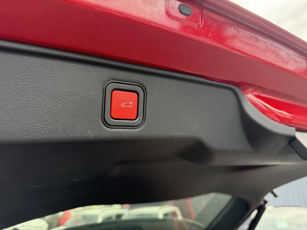 Bouton rouge d'ouverture électrique du hayon sur le bord intérieur du coffre d'une FIAT 600 rouge 2024.