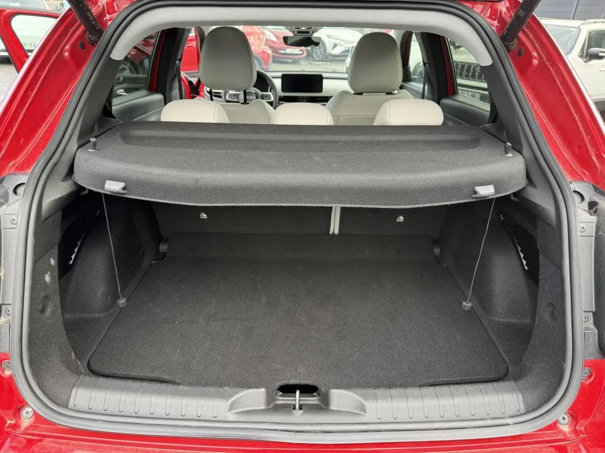 Coffre ouvert vu de l'arrière d'une FIAT 600 rouge, avec banquette arrière ivoire et cache-bagages déployé.