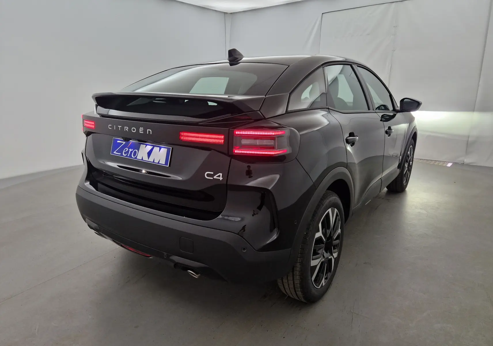 Vue 3/4 arrière droite d'une Citroën C4 noire 2025 avec feux arrière LED allumés et jantes alliage noires.