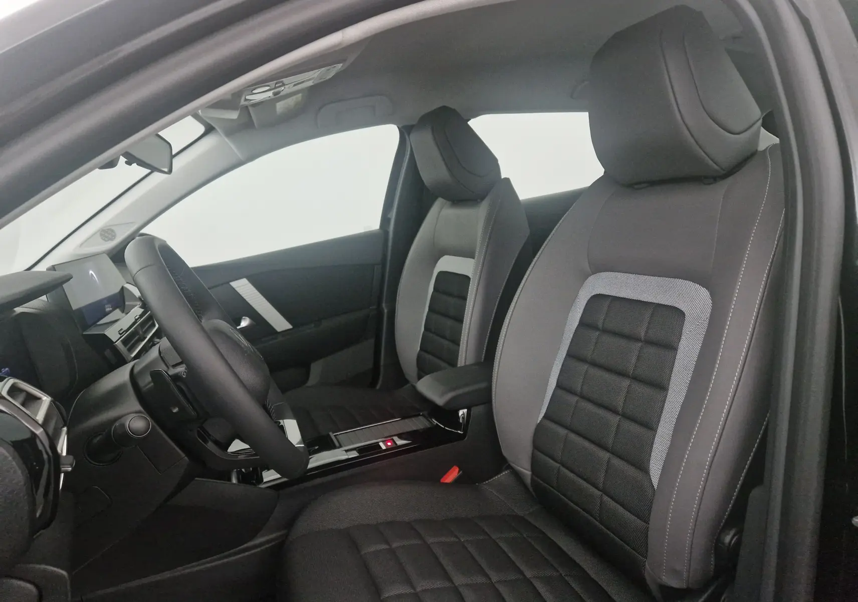 Vue intérieure côté conducteur de la Citroën C4 2025 noire, sièges tissu noir et gris avec console centrale moderne.