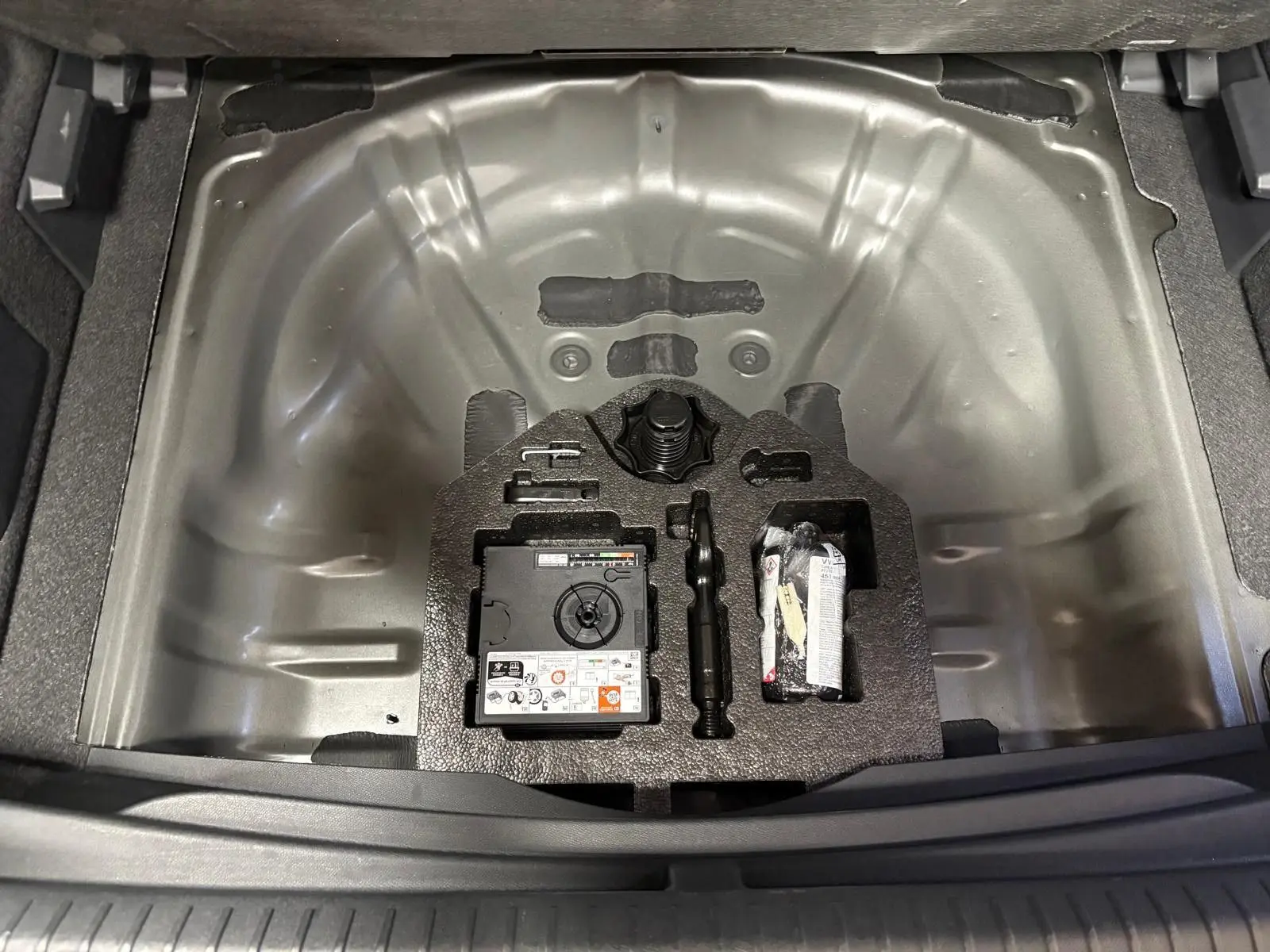 Coffre ouvert en vue plongeante du CUPRA Formentor noir minuit, montrant le rangement pour roue de secours et kit de réparation.