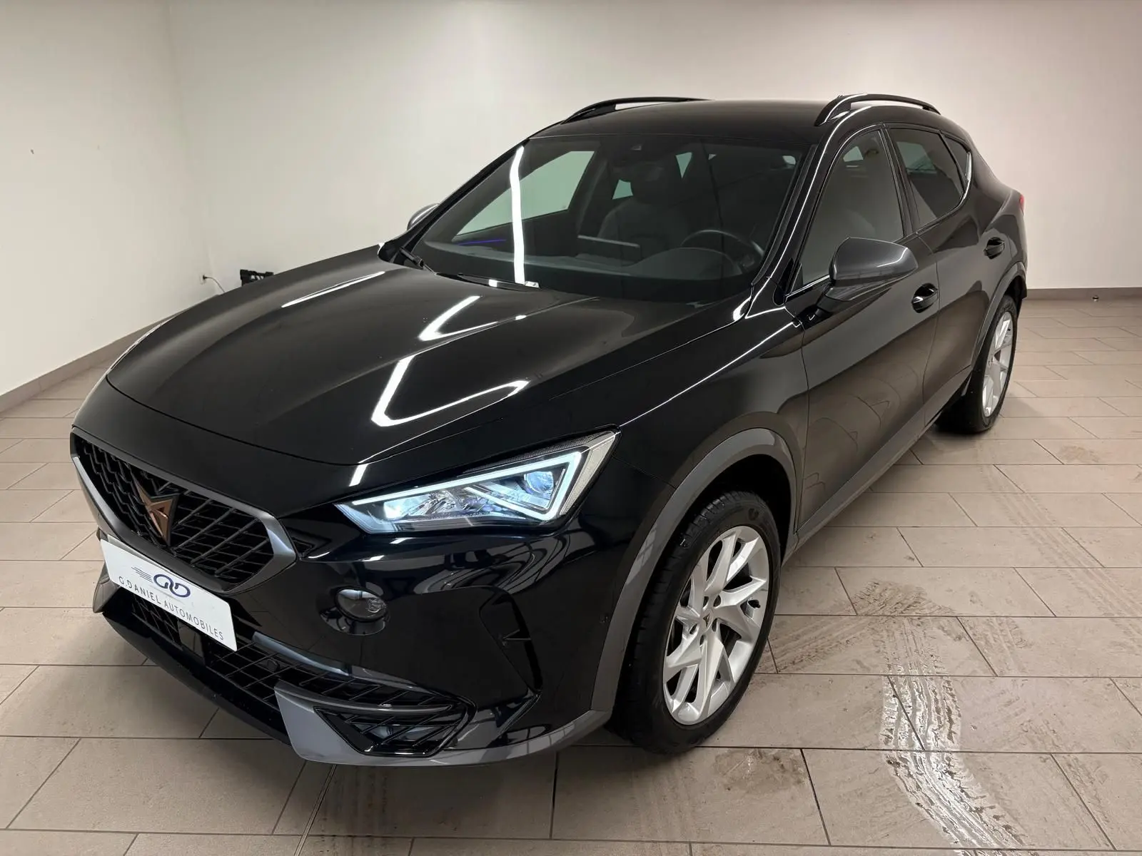 CUPRA Formentor noir minuit en 3/4 avant droit, avec phares allumés et jantes argentées visibles en intérieur clair.