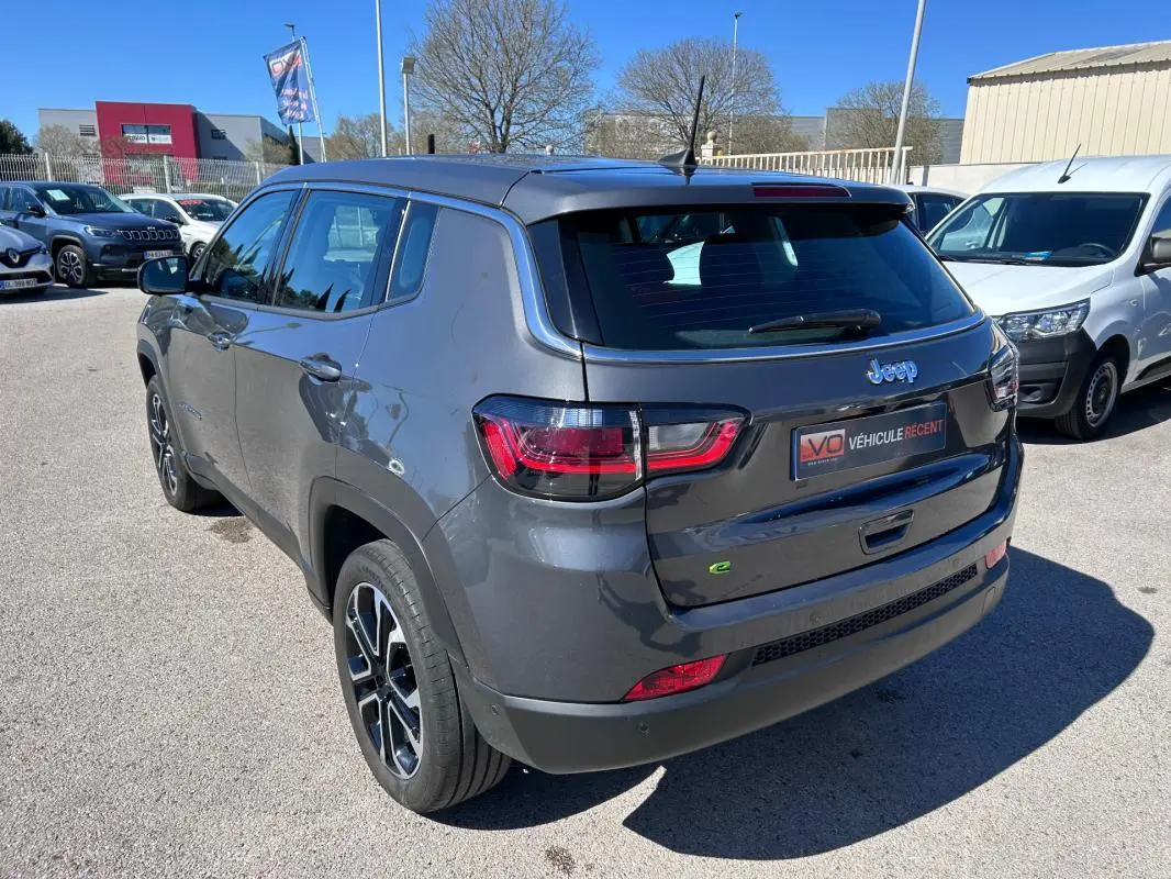 Jeep Compass gris 3/4 arrière droit, jantes alliage 18 pouces, feux arrière LED et badge e-Hybrid visible.