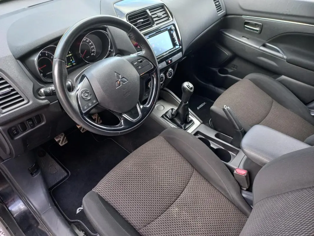 Vue intérieure côté conducteur du Mitsubishi ASX 2020 noir, montrant le volant, la boîte manuelle et l'accoudoir central.
