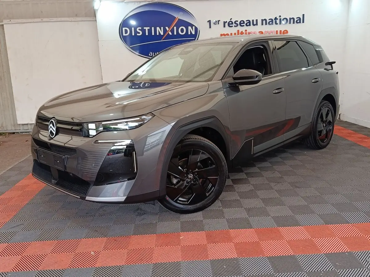 Citroën C5 Hybride gris foncé vue 3/4 avant avec jantes noires et calandre distinctive en intérieur showroom.