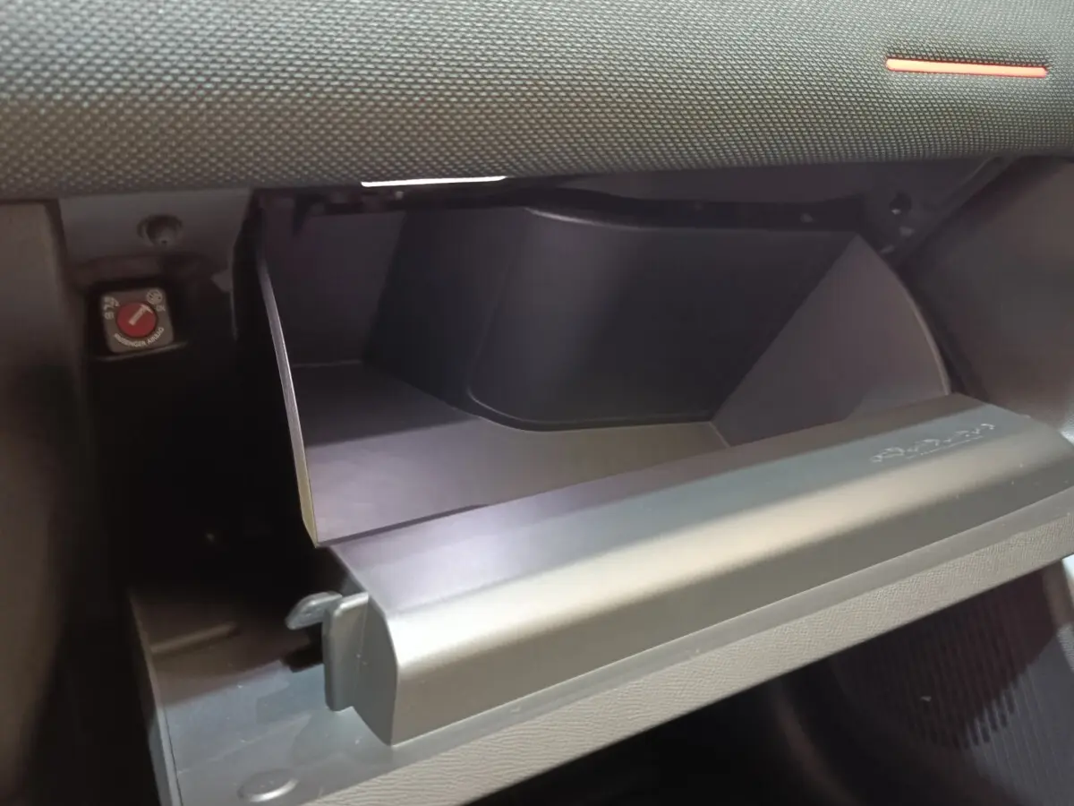 Gros plan sur la boîte à gants ouverte de la Citroën C5 Hybride 2026, intérieur noir mat et texture sobre.