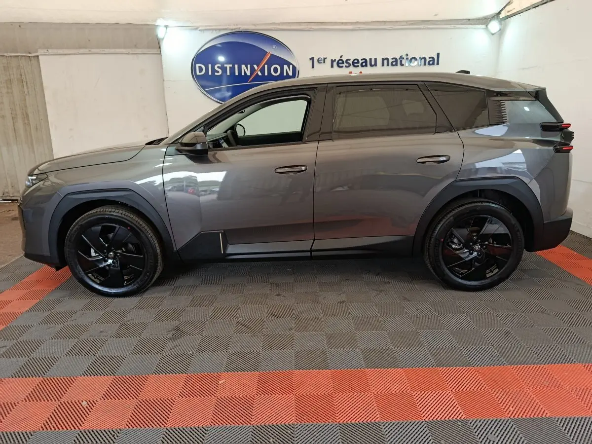 Vue de profil côté gauche d'un Citroën C5 Hybride gris foncé avec jantes noires dans un showroom.