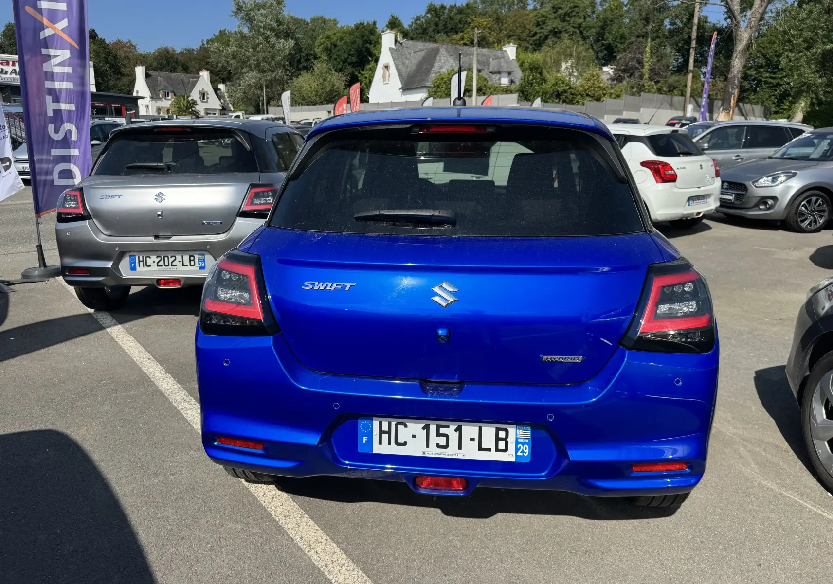 Vue arrière d'une Suzuki Swift 1.2 Privilège Hybrid bleue, stationnée en extérieur sur un parking.
